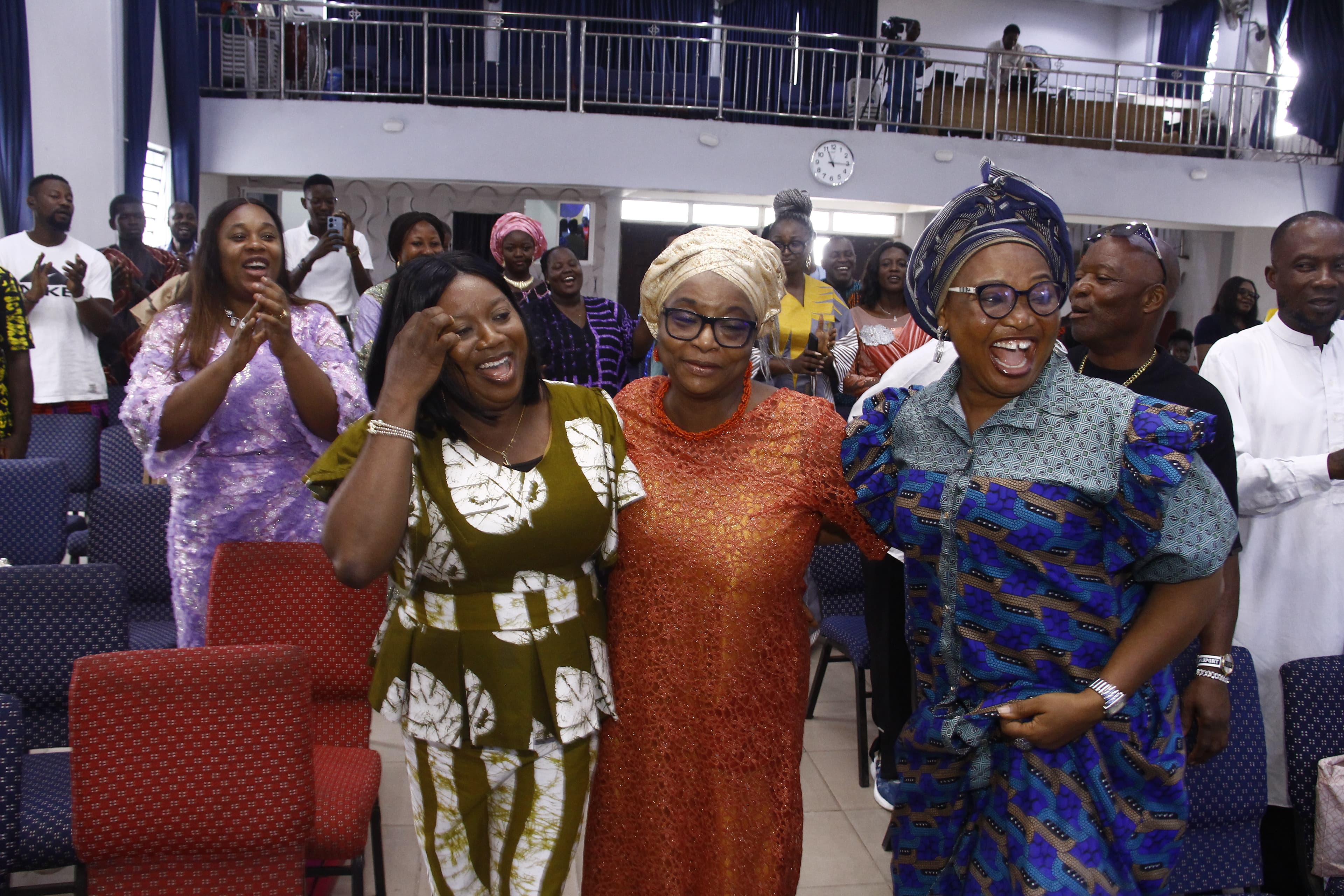 Three women laughing together arm-in-arm in colorful outfits