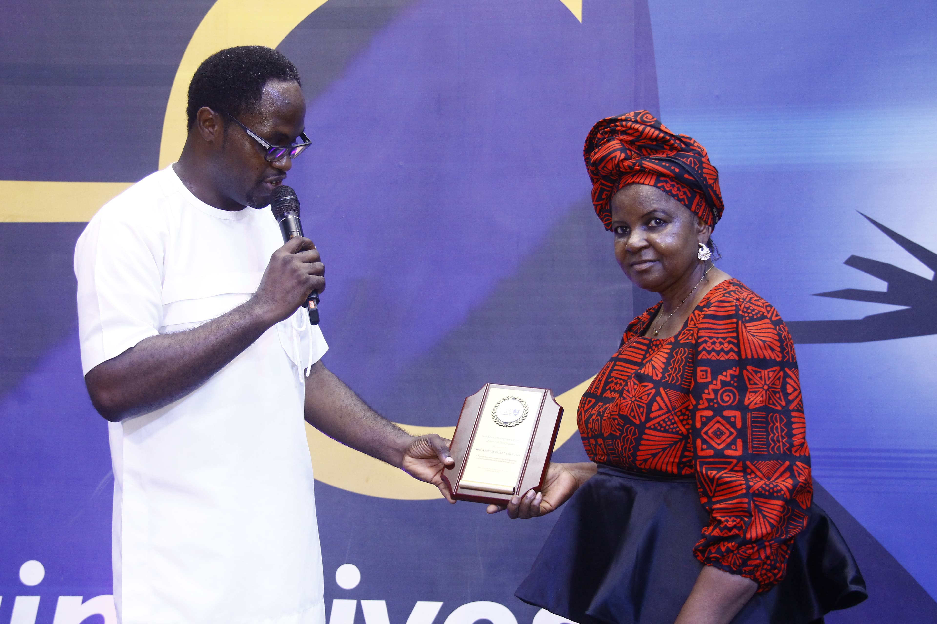 Award presentation to woman in red African print headwrap