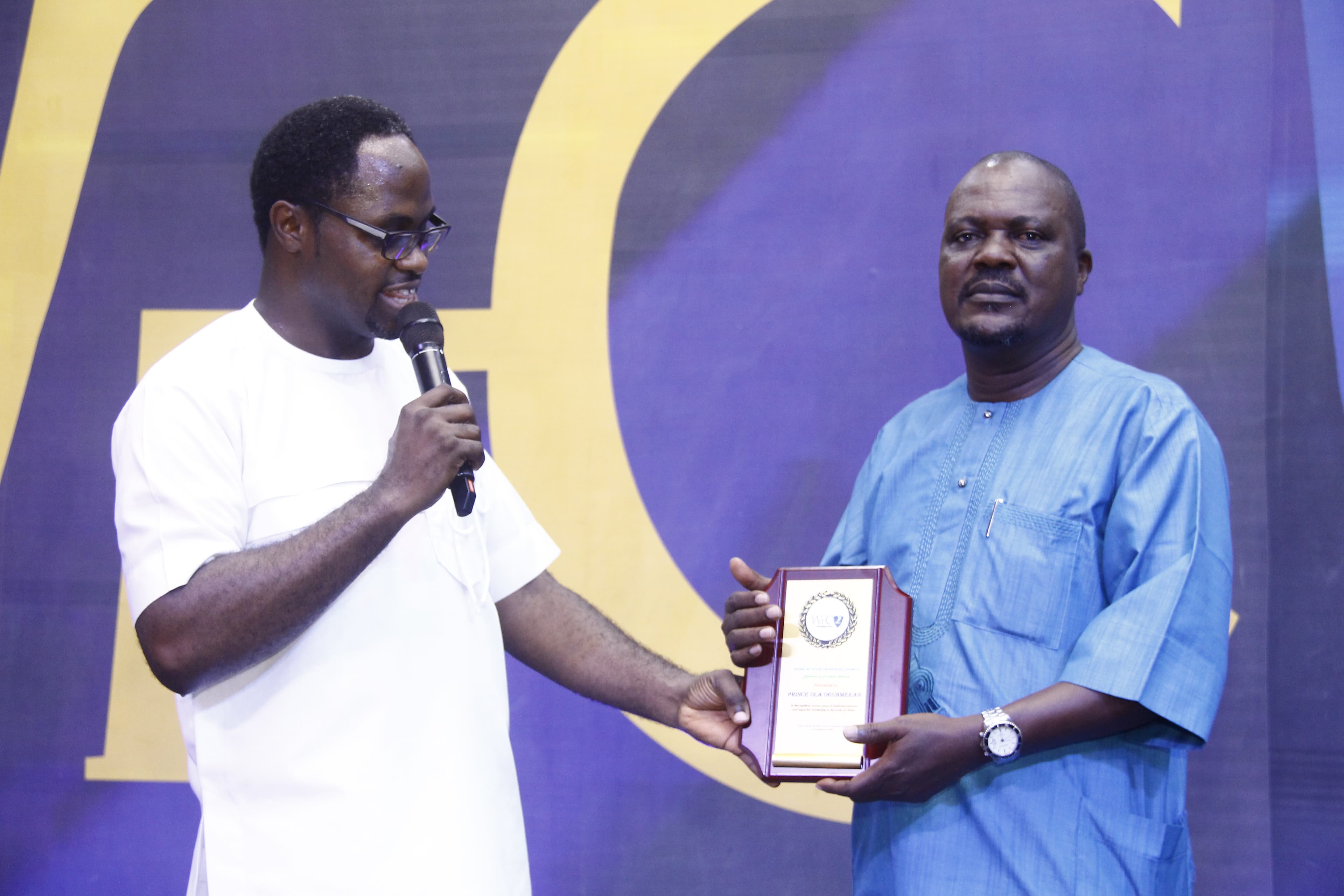 Man receiving plaque in blue agbada on stage