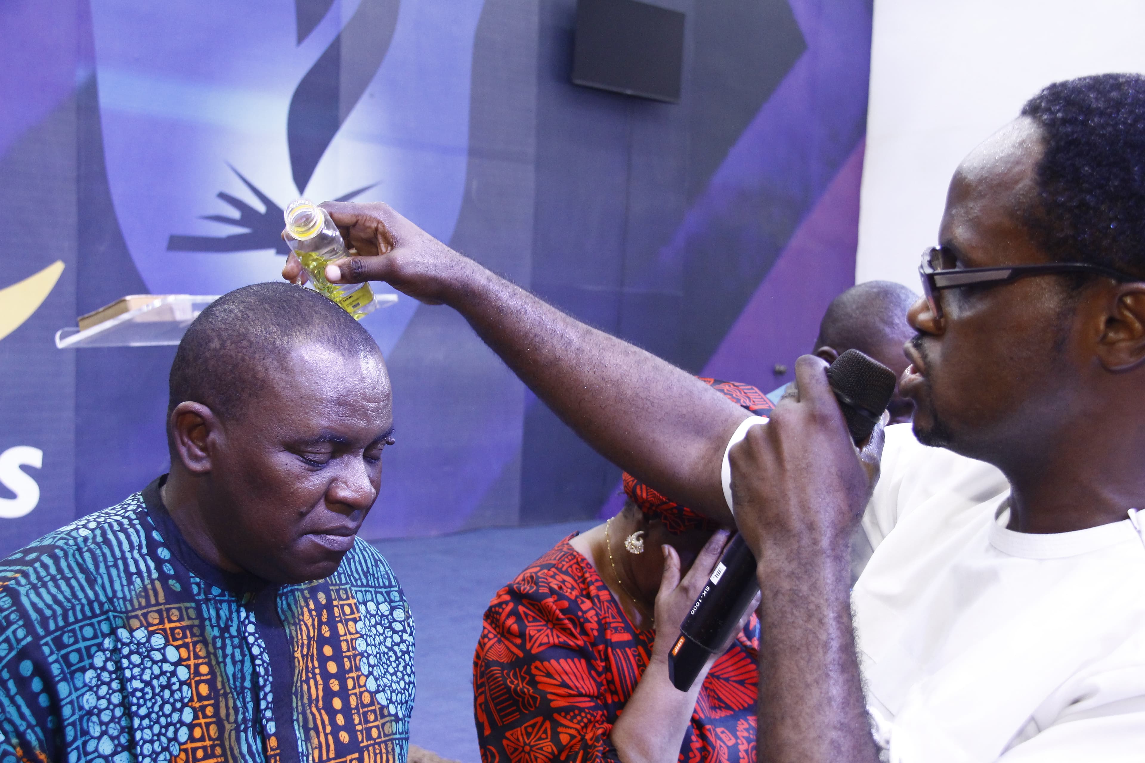 Pastor anointing man with oil on stage in purple light