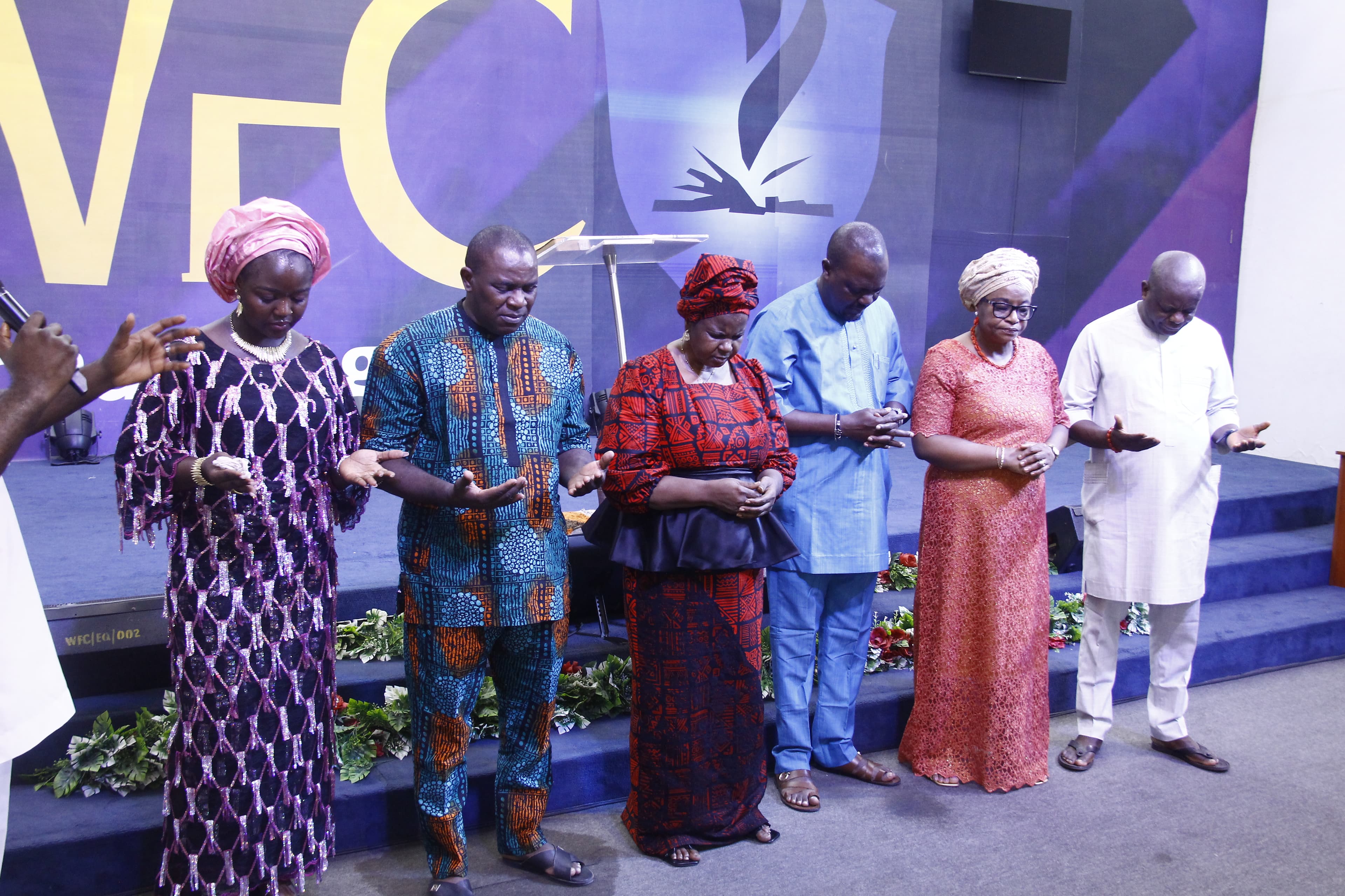 Church leaders standing in prayer with bowed heads on stage