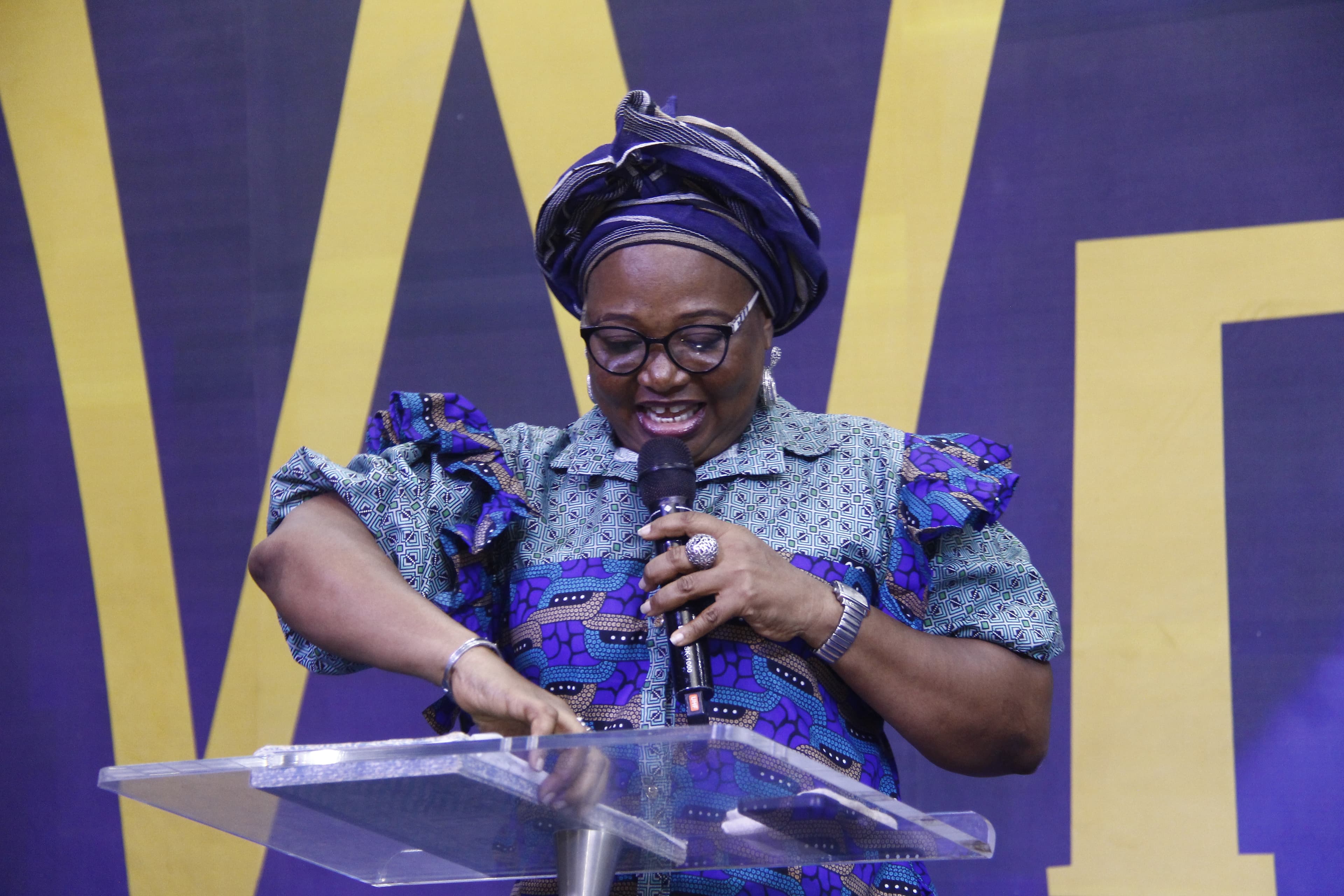 Woman speaking at podium in blue African print and headwrap